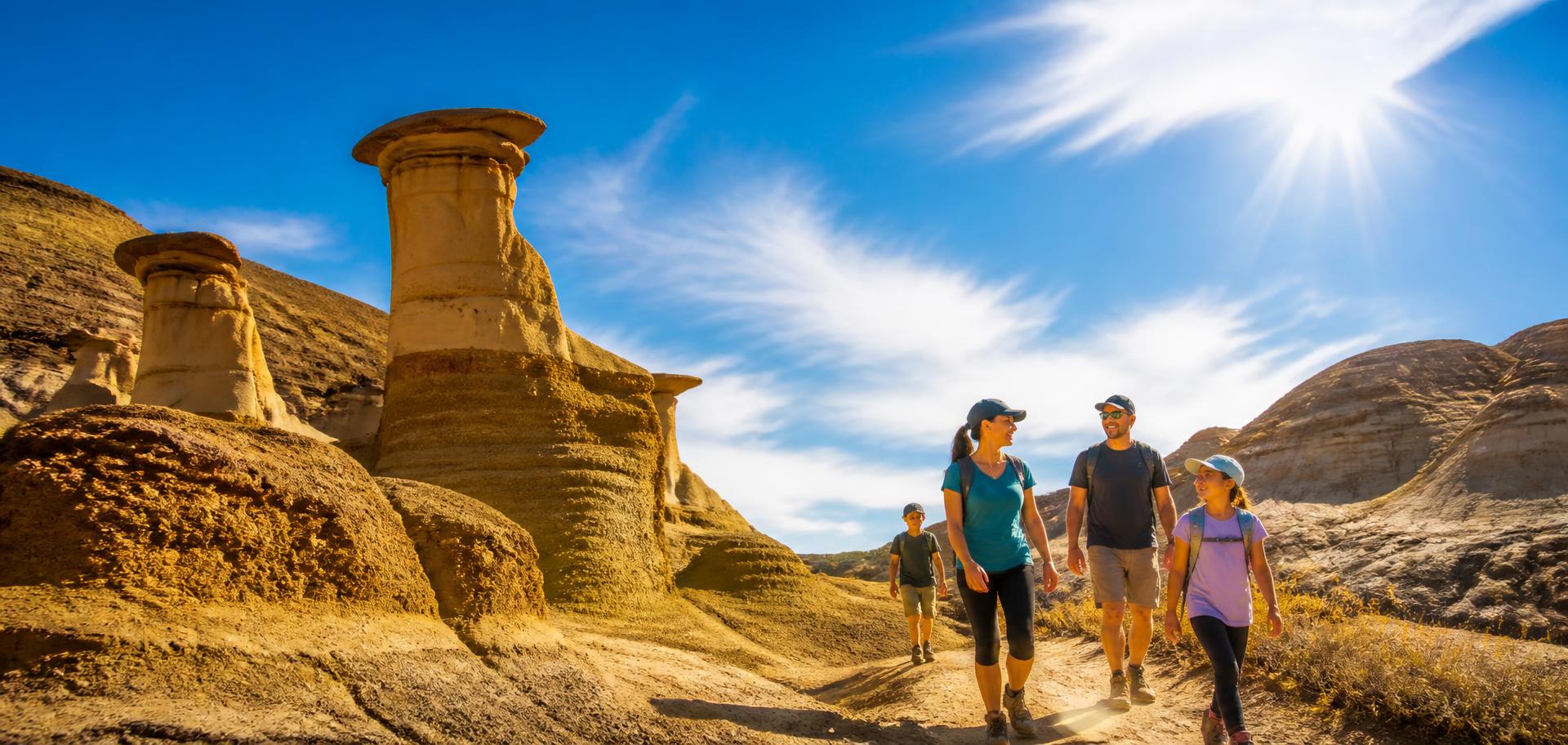 A smiling family hiking among the Drumheller hoodoos under a vivid blue Alberta sky