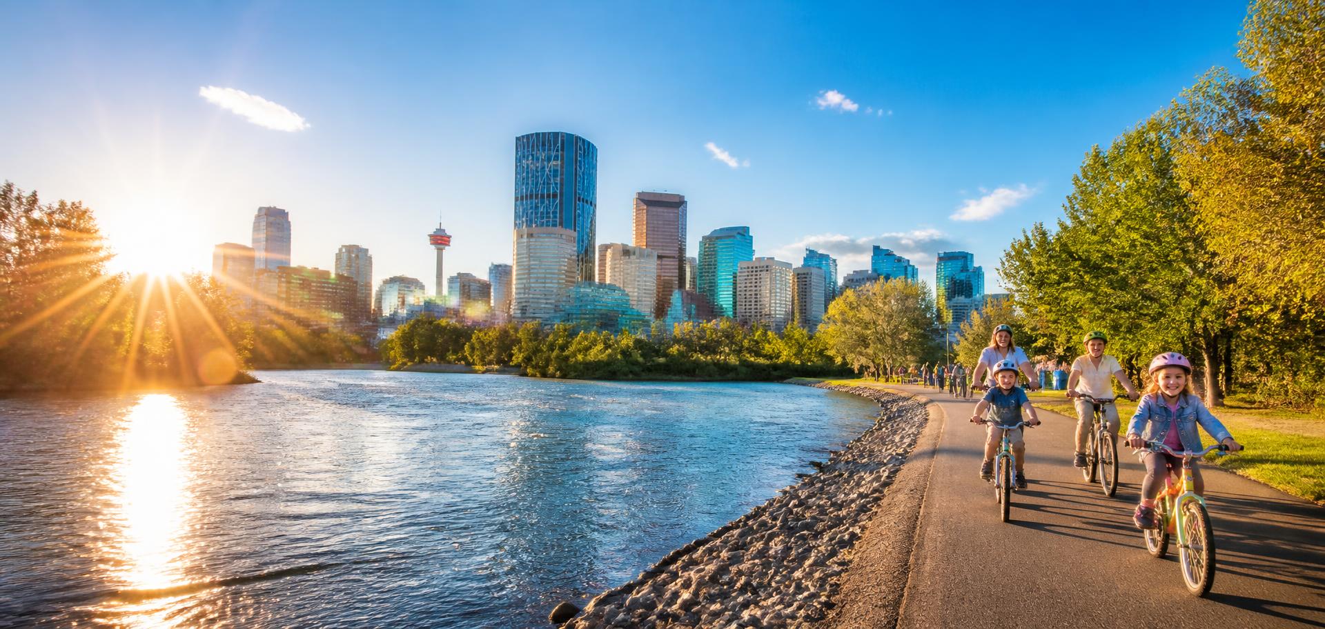 Families cycling along the Bow River pathway with the sunlit Calgary skyline behind