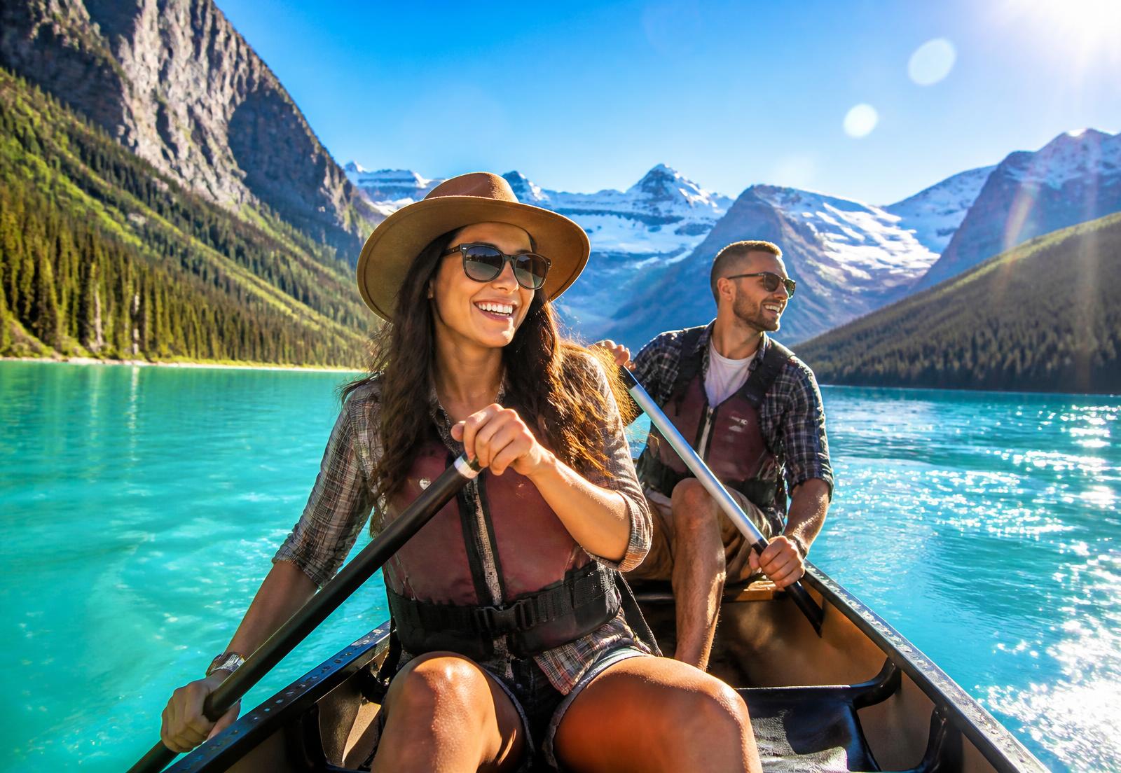 Two smiling paddlers canoeing on a turquoise Alberta mountain lake in bright sunshine
